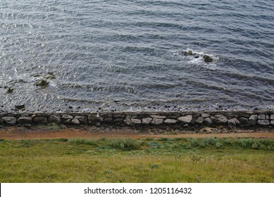 Distant view of beach side with large stones and green grass during daytime on sunny day
