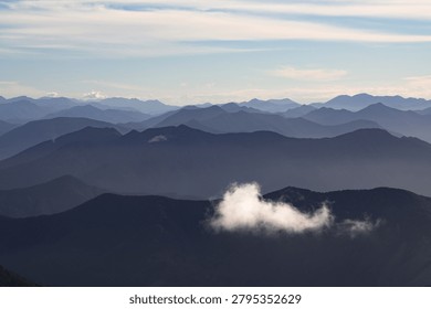 Distant view of a mountain range with multiple peaks under cloudy sky seen from an elevated position with rolling terrain in the foreground. New Zealand highland panorama.