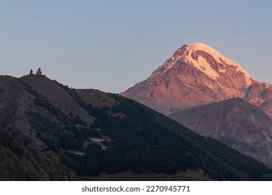 Distant view on Gergeti Trinity Church in Stepansminda, Georgia. The church is located the Greater Caucasian Mountain Range. Clear sky above the snow-capped Mount Kazbegi in the back. Sunrise, sunset - Powered by Shutterstock