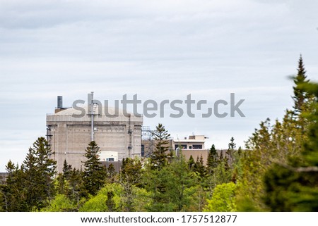 a distant view of the Point Lepreau Nuclear Generating Station through the woods. Most of the reactor is visible but the bottom is obscured by trees.