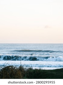 Distant view of a surfer riding a breaking ocean wave during a peaceful sunset.
