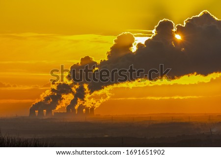 Distant view from the Yorkshire Wolds, UK of a Power Station's cooling towers near Drax in North Yorkshire. The sun is setting behind the water vapour trail on a cold winter's night. Backlit image. 