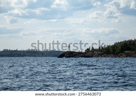 Distant white navigation beacon on a rocky promontory of a Ladoga skerry. Dark blue rippling water and forested shores viewed from a summer boat trip.