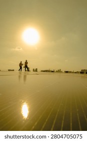 Distant workers against the setting sun cross a rooftop solar farm as the sun sets on a rooftop solar farm, highlighting green technology, occupational safety and the daily work.