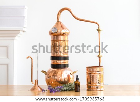 Distilling apparatus alembic with esential oil flowers at the wooden table.