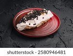 A distinct dessert features a creamy layer topped with black caviar on a textured dark surface, served on a round red plate. The contrast of colors enhances its visual appeal.