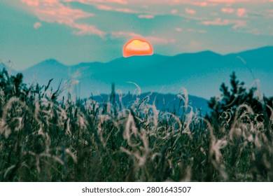 Distorted orange sun setting over mountains and a field of fescue grass during a heatwave
