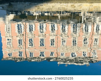 Distorted reflection of pink building on water surface in bright daylight.