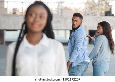Distracted african american guy turning around and looking to another woman while walking with his girlfriend