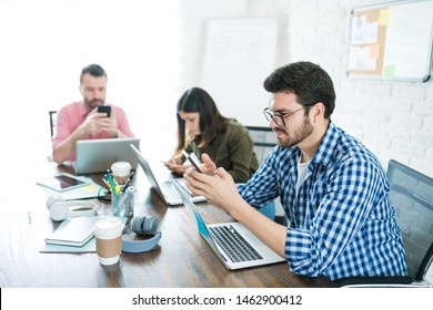 Distracted Business Colleagues Using Smartphones While Sitting At Conference During Meeting In Workplace