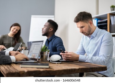 Distracted Businessman Using Mobile Phone In Meeting