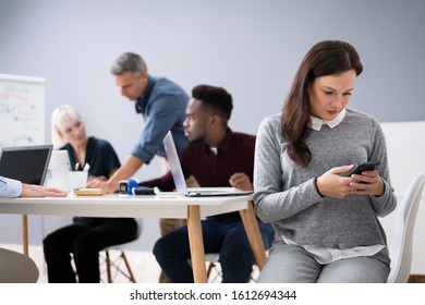 Distracted Businesswoman Using Mobile Phone In Meeting