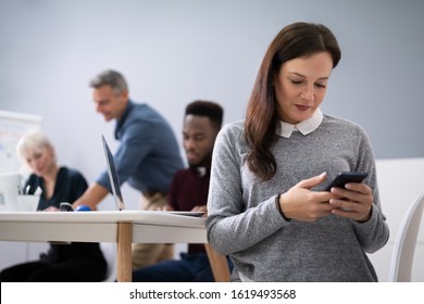 Distracted Businesswoman Using Mobile Phone In Meeting