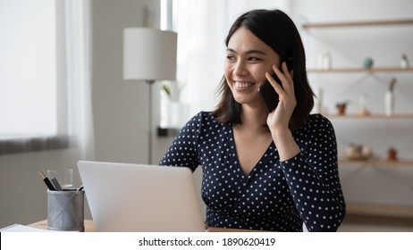 Distracted from computer work happy millennial korean asian woman holding pleasant mobile phone conversation with friends, smiling young female vietnamese worker consulting client by cellphone. - Shutterstock ID 1890620419