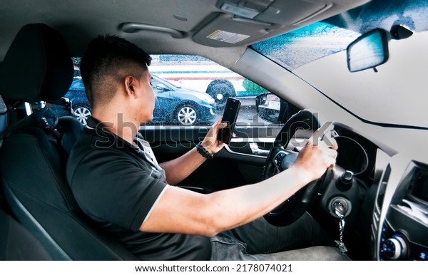 Distracted driver using the cell phone while\
driving, Man using his phone while driving, Person holding the cell\
phone and with the other hand the steering wheel, Concept of\
irresponsible\
driving