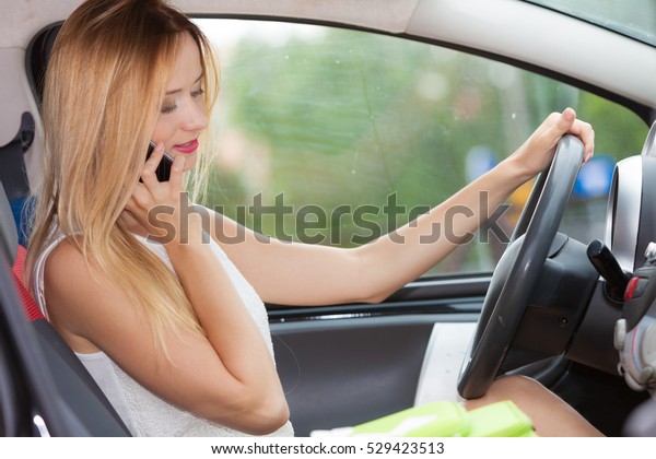 Distracted driver. Young attractive\
woman using mobile phone, talking while driving the\
car.