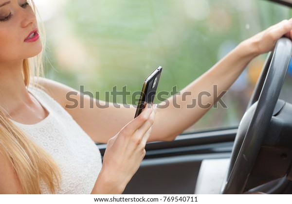 Distracted driver. Young\
attractive woman using mobile phone, texting or read message while\
driving the car.