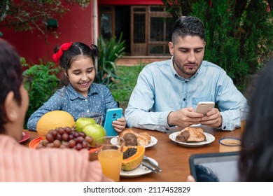 Distracted Family Using Mobile And Having Breakfast In Table Outside