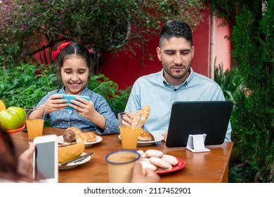 Distracted Family Using Mobile, Tablet And Having Breakfast In Table Outside