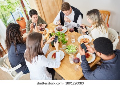 Distracted friends all look at their smartphone while having lunch together at the table