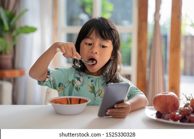 Distracted Kid Using Mobile Phone While Having Breakfast On The Table