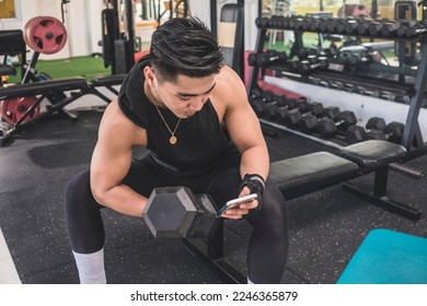 A distracted man checking his social media feed on his cellphone while doing a set of seated concentration dumbbell curls at the gym. - Shutterstock ID 2246365879