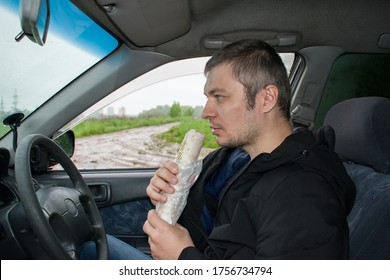 Distracted Man In Vehicle. Bad Unhealthy Habit. Junk Food Go. Hungry Adult Man Starving And Driving His Car While Eating Fast Food.