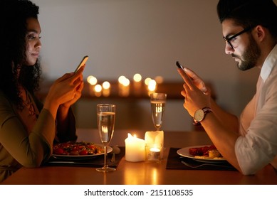 Distracted Over Dinner. Shot Of A Young Couple Texting On Their Phones While Out For Dinner.