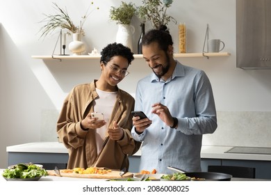 Distracted from preparing healthy food joyful laughing young African American married family couple renters using smartphones, watching funny video with recipes online, communicating in kitchen. - Powered by Shutterstock