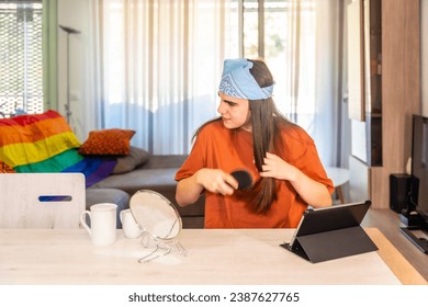 Distracted transgender person arranging the long hair at home sitting on a table with a digital tablet and a mirror - Powered by Shutterstock