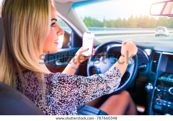 Distracted young business\
woman driver using a smartphone and texting while driving a car on\
a highway