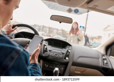 Distracted young male driver looking at the screen of his mobile phone while running over a pedestrian. Technology and transportation concept. Selective focus on hand with smartphone. Horizontal shot