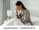 Distraught lady sitting on bed, crying and wiping away tears with tissue, suffer from sadness or emotional distress in bedroom