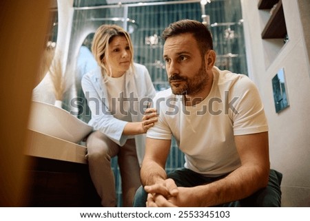 Distraught man being consoled by his wife while sitting in the bathroom. 