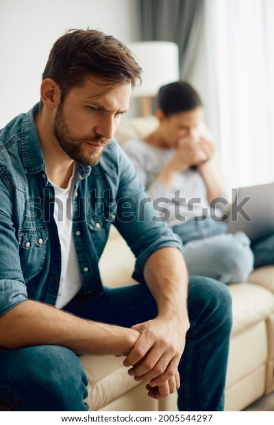 Distraught man sitting\
on the sofa and thinking while having relationship problems with\
his wife at home. 