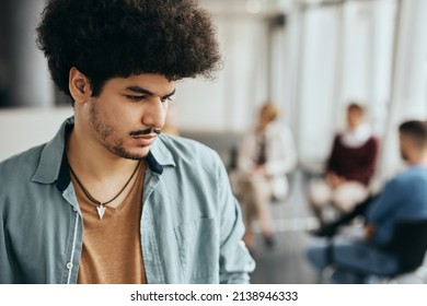 Distraught Muslim Man Thinking Of Something While Standing Apart From Attenders Of Group Therapy At Mental Health Center.