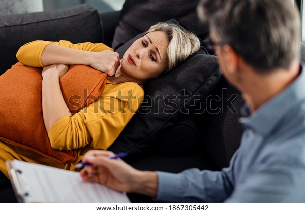 Distraught\
woman talking to a mental health professional while lying down on\
psychiatrist\'s couch and hugging a pillow.\
