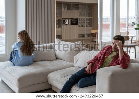 Distressed and angry couple sits on opposite ends of couch after fight, ignoring each other amidst manipulative and abusive family dynamics. Toxic silence and manipulation in couple relationship