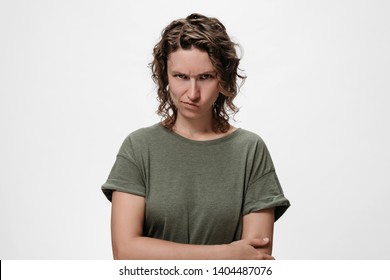 Distressed Angry Offended Curly Woman Purses Lips, Looks With Jealousy And Regret, Keeps Hands Crossed Over Chest, Tells About Unfair Things, Feels Offended, Isolated On White Wall