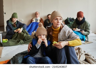 Distressed Caucasian Refugee Family Eating Sandwiches While Hiding In Shelter On Floor Covered With Blankets