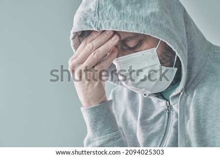 Distressed frightened covid-19 make patient in self-isolation wearing hooded shirt and protective face mask