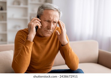 Distressed grey-haired senior man sitting on couch in living room interior, have phone conversation at home, hear bad news or fighting with wife, touching head, closeup, copy space - Powered by Shutterstock