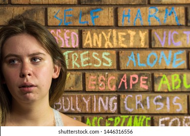 Distressed looking teenage girl in front of a brick wall with words written in chalk