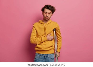 Distressed Male Feels Pain In Ribs, Suffers From Fracture After Domestic Accident, Looks Sadly Down, Thinks Over Treatment, Poses With Crutch Under Arm, Fell While Snowboarding During Recreation Time