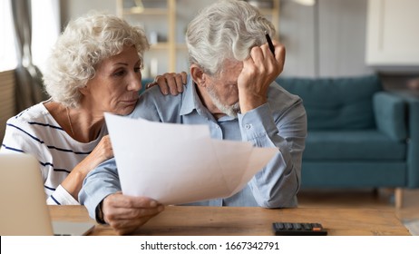 Distressed mature 60s husband and wife sit at table calculate manage household expenses having problems with finances, upset pensioners frustrated troubled with paying bills expenditures