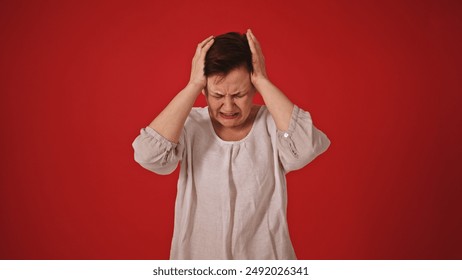 Distressed Senior Woman Covering Ears to Block Out Loud Noise on Red Background - Powered by Shutterstock