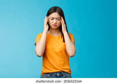 Distressed tired asian woman dark haircut cringe touch temples, suffer huge migraine need painkillers, painful headache, feel dizzy, stand blue background intense drained - Shutterstock ID 2036523164