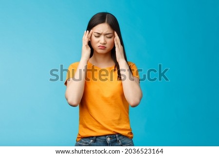 Distressed tired asian woman dark haircut cringe touch temples, suffer huge migraine need painkillers, painful headache, feel dizzy, stand blue background intense drained