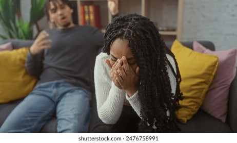 A distressed woman covers her face with hands beside a frustrated man on a couch, depicting a couple's argument in a living room. - Powered by Shutterstock
