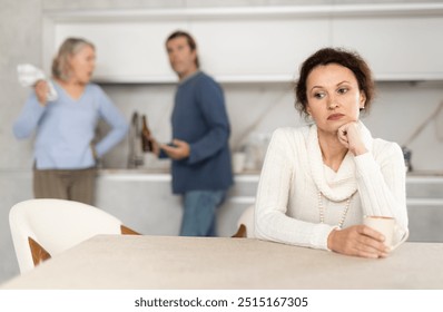 Distressed woman is present during quarrel between her husband and elderly female mom. Mature woman and son-in-law swear and insult each other - Powered by Shutterstock